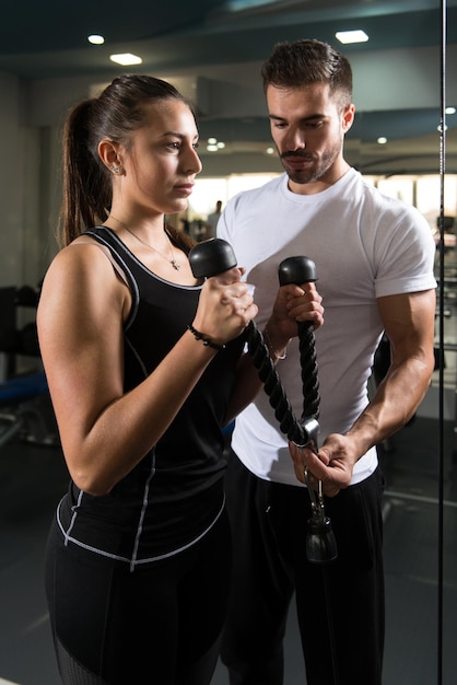 Femme avec un entraîneur personnel au biceps dans la salle de gym