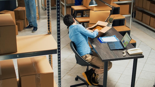 Femme entrepreneur analysant les produits des racks d'entrepôt, regardant les marchandises et les boîtes avant d'expédier la commande de marchandises. Jeune femme travaillant dans une salle de stockage avec chaîne d'approvisionnement. Prise de vue au trépied.