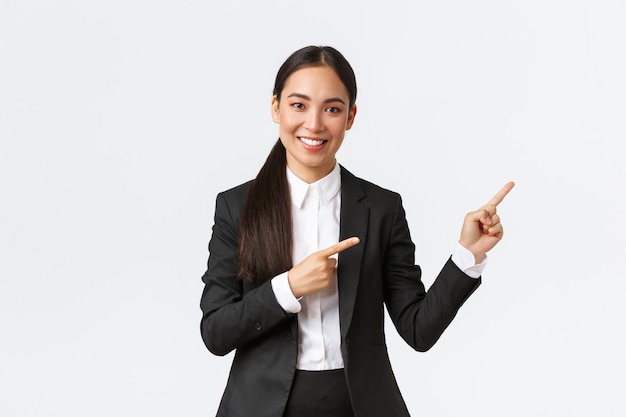 Une femme entrepreneur asiatique confiante, une vendeuse en costume présente le produit, montrant la place aux clients. Femme d'affaires souriant et pointant du doigt vers la bannière, debout sur fond blanc