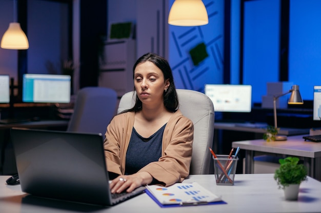 Femme entrepreneur concentrée travaillant sur son ordinateur portable faisant du surmenage pour terminer une date limite. Femme intelligente assise sur son lieu de travail pendant les heures tardives de la nuit faisant son travail.