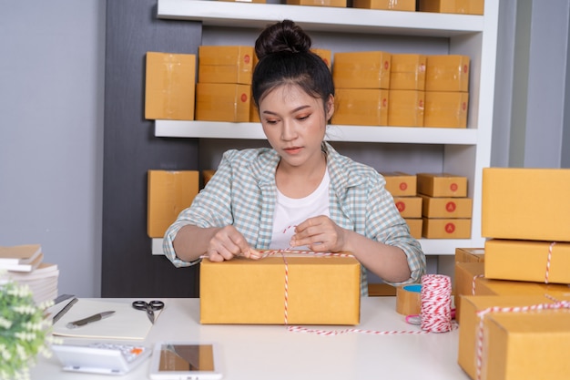 Femme entrepreneur nouant des cordes et des produits d&#39;emballage dans une boîte à colis