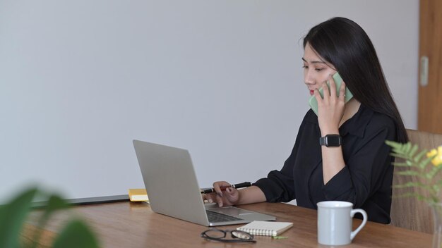 Femme entrepreneur occupée utilisant un ordinateur portable et parlant sur un téléphone portable avec son partenaire commercial