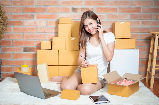 Femme entrepreneur propriétaire PME entreprise vérifie la commande avec téléphone, ordinateur portable et boîte d'emballage pour envoyer son client