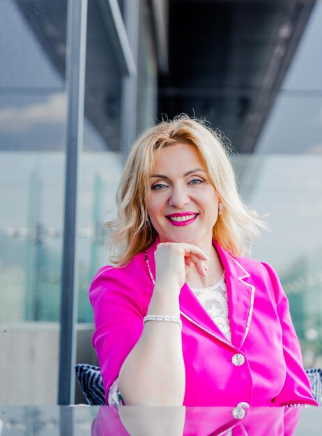 Femme entrepreneur prospère dans une veste magenta posant sur la terrasse d'un café dans un centre d'affaires. Concept de représentation de femme d'affaires