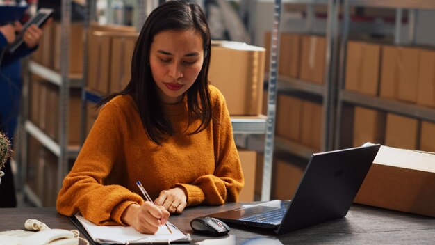 Femme entrepreneur vérifiant les produits en stock sur pc, utilisant un ordinateur portable pour travailler sur la distribution et la gestion des commandes. Femme faisant de la planification financière pour le développement des affaires. Prise de vue à main levée.