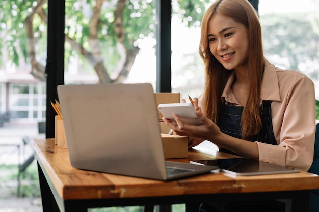Femme entrepreneure asiatique utilisant une calculatrice avec un crayon à la main calculant les dépenses financières au bureau à domicile livraison de boîtes d'emballage du marché en ligne