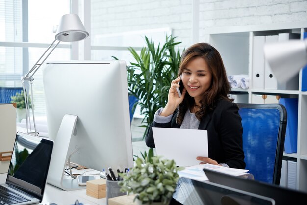 Femme entrepreneure assez souriante parlant au téléphone avec un collègue d'un autre département quand regardez...