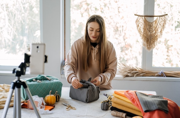 Une femme enveloppe un cadeau furoshiki dans un style zéro déchet et enregistre une master class de vlog sur un furoshiki de téléphone portable