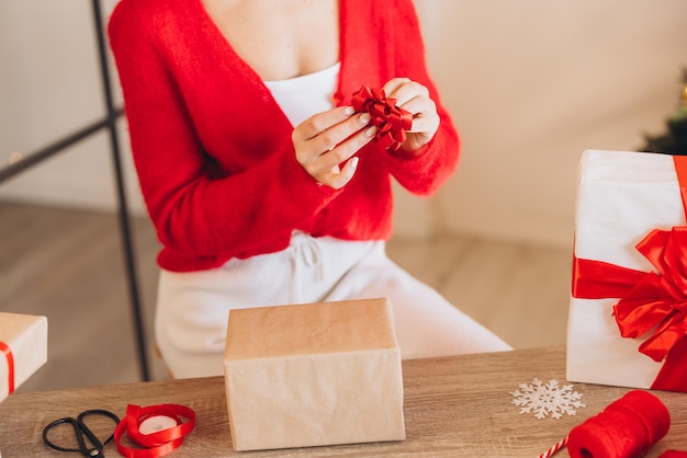 Une femme enveloppe des cadeaux avec des rubans rouges à Noël