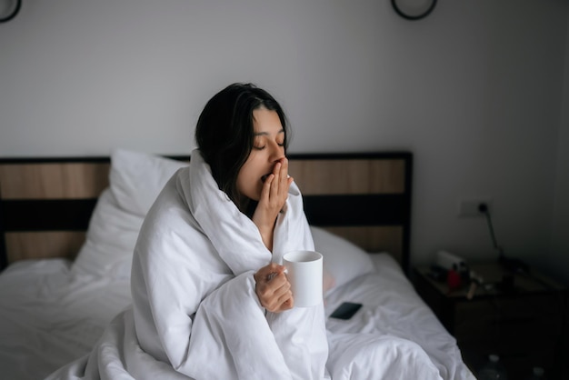 Femme enveloppée dans une couverture et tenant une tasse