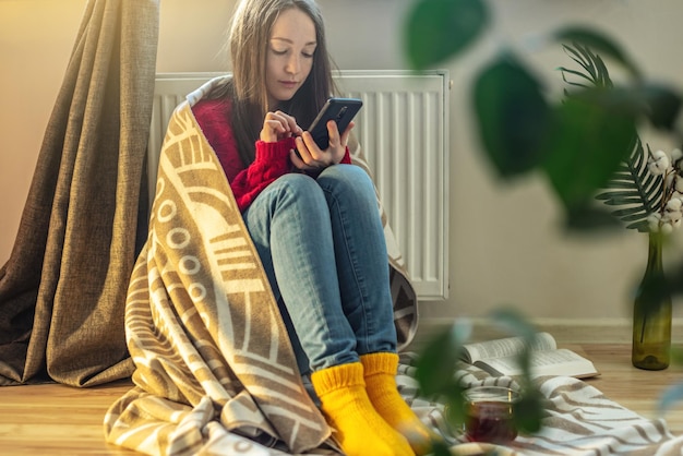 Une femme enveloppée dans un plaid est assise sur le sol et se réchauffe près d'un radiateur chaud Crise des ressources énergétiques