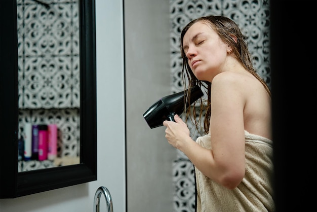 Femme enveloppée dans une serviette séchant les poils debout dans la salle de bain routine hygiénique matinale féminine et ha