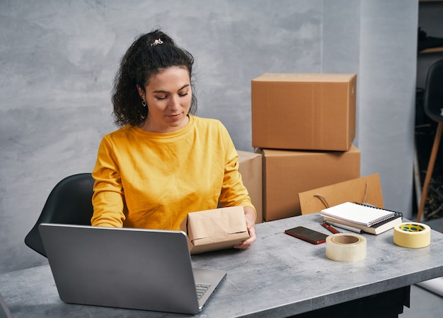 Femme envoyant un colis à l'aide de son ordinateur portable travaillant à domicile