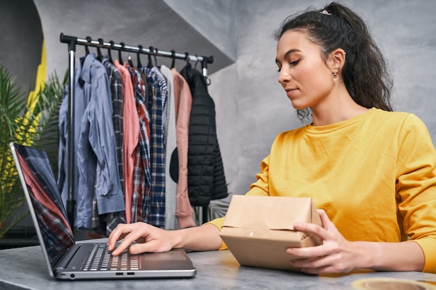 Femme envoyant un colis à l'aide de son ordinateur portable travaillant à domicile