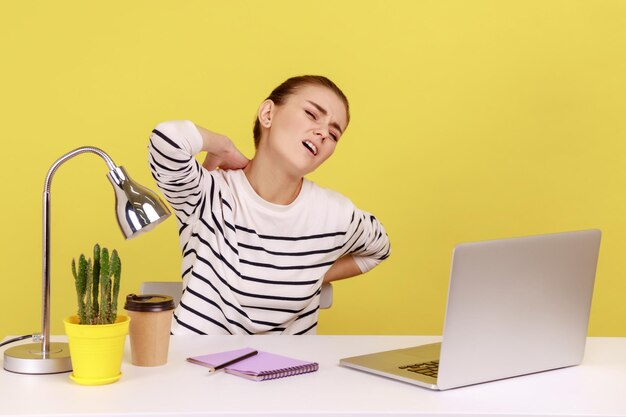 Une femme épuisée assise sur le lieu de travail et souffrant de terribles douleurs au cou et au dos a l'air fatiguée