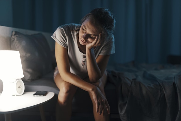 Femme épuisée souffrant d'insomnie, elle est assise sur le lit et réfléchit