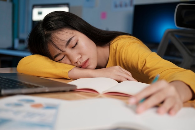 Femme épuisée et stressée assise au bureau et faisant des heures supplémentaires, elle est surchargée de travail.