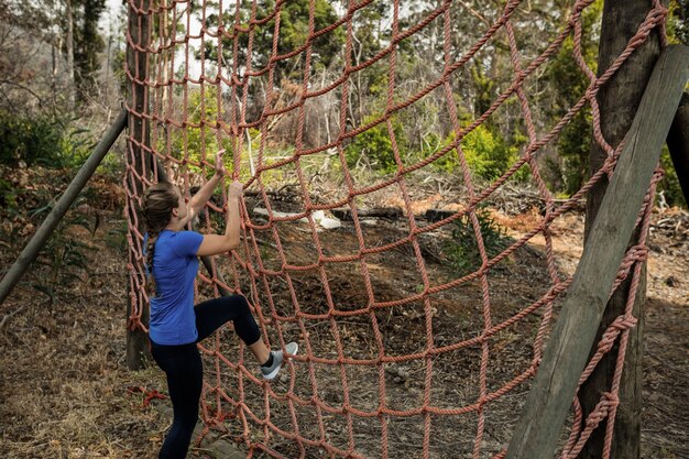 Femme escalade un filet pendant la course d'obstacles