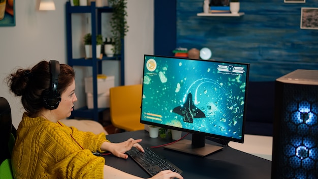 Femme eSports professionnelle jouant à des jeux vidéo sur un PC puissant et moderne. Jeune joueur professionnel jouant à un jeu de tir se produisant sur un ordinateur dans une pièce élégante pendant un tournoi de jeu