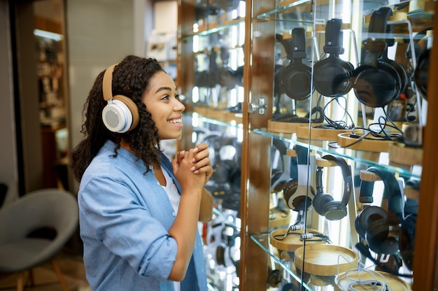 Femme essayant des écouteurs dans le magasin de système de haut-parleurs. Personne de sexe féminin dans la boutique audio, vitrine avec écouteurs, acheteur en magasin multimédia