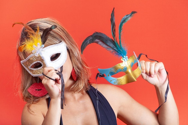 Une femme essayant des masques vénitiens colorés isolés sur un fond orange.