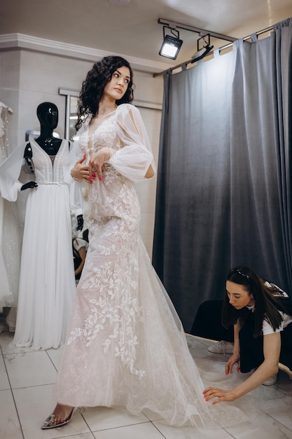 Femme essayant une robe de mariée dans un magasin avec une assistante féminine