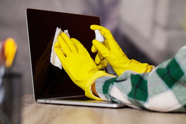 Femme essuie l'ordinateur portable de la poussière dans le bureau à la table