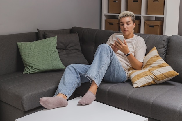 Une femme est allongée sur un canapé avec un smartphone dans un intérieur de maison minimaliste