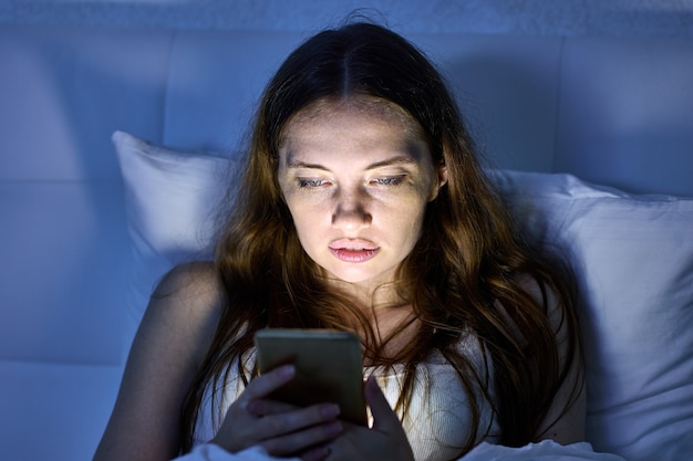 Une femme est allongée dans son lit et utilise son téléphone le soir