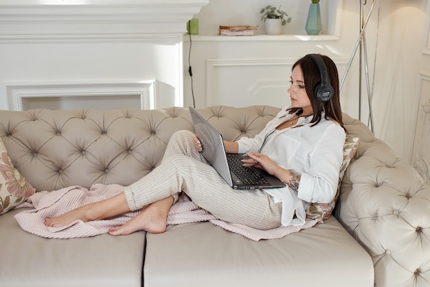 Une femme est allongée à la maison sur le canapé avec des écouteurs et écoute de la musique. Journée de repos à la maison, détente et repos