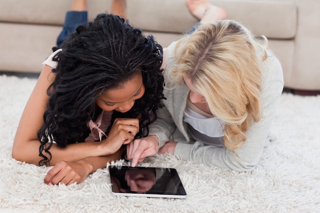 Une femme est allongée sur le sol à l&#39;aide d&#39;une tablette tandis que son amie regarde