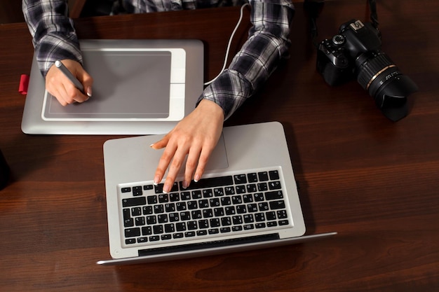 La femme est assise au bureau et retouche des photos sur un ordinateur portable