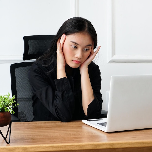 Une femme est assise à un bureau avec un ordinateur portable et une plante sur le mur derrière elle.