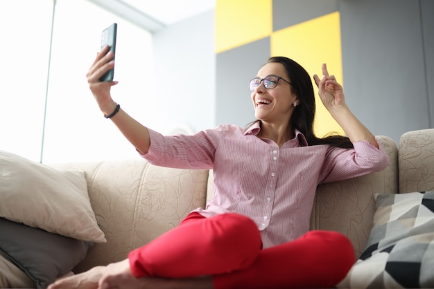 Une femme est assise sur un canapé et, avec le sourire, accueille son interlocuteur lors de la diffusion vidéo