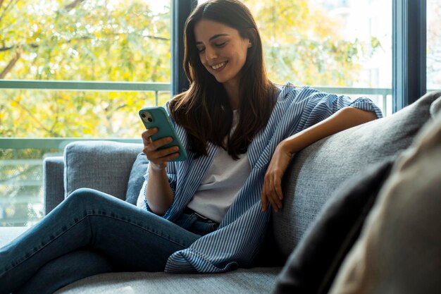 une femme est assise sur un canapé avec un téléphone à la main