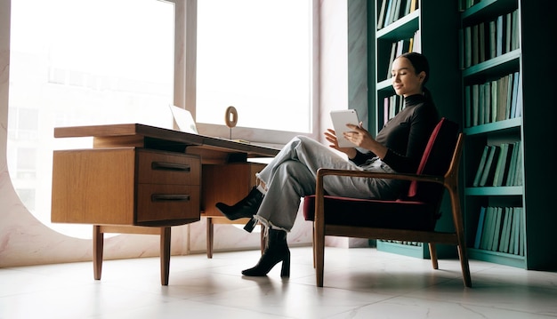 Une femme est assise sur une chaise devant un bureau avec un livre et une bibliothèque avec une bibliothèque derrière elle