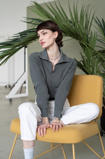 Une femme est assise sur une chaise jaune devant une plante