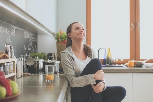 Une femme est assise sur le comptoir de la cuisine devant un verre de jus d'orange.