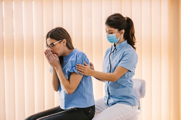 Une femme est assise dans le cabinet du médecin et tousse d'une maladie pulmonaire pendant qu'un médecin examine