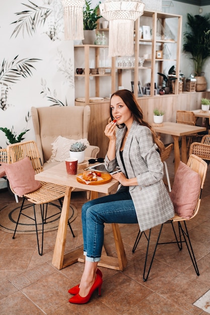 Une femme est assise dans un café et mange des fraises. Une fille avec des fraises dans ses mains dans un café.