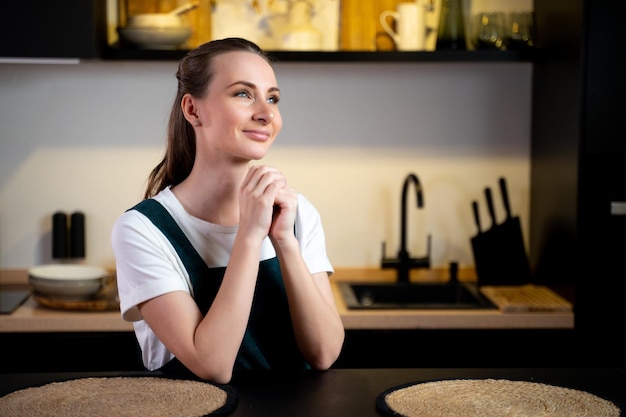 Une femme est assise dans une cuisine, les mains jointes en prière.