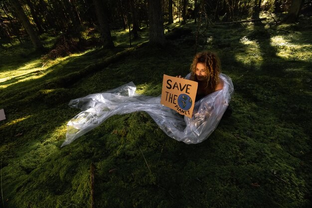 Une femme est assise dans une forêt tenant une pancarte qui dit sauvez la terre.