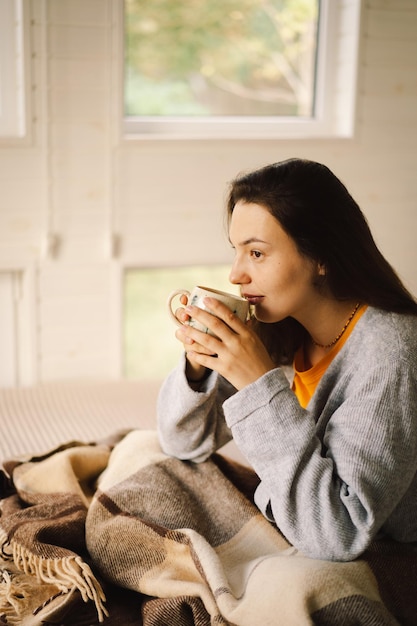 Une femme est assise dans une pièce confortable en train de profiter d'un café et de lire un livre pendant une matinée relaxante