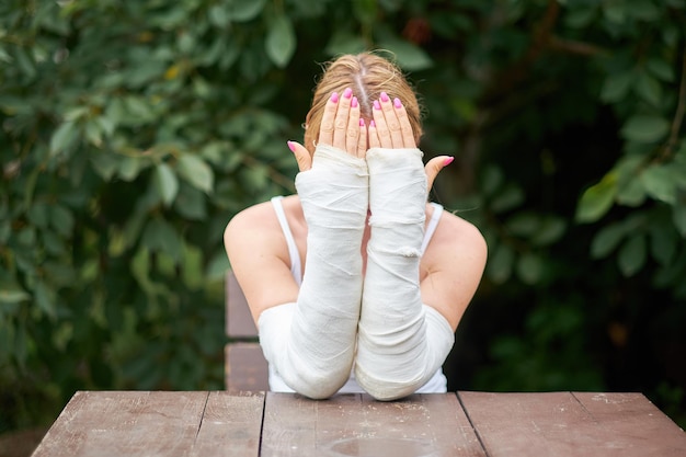 Une femme est assise avec les deux mains dans le plâtre après une blessure et se couvre le visage de chagrin