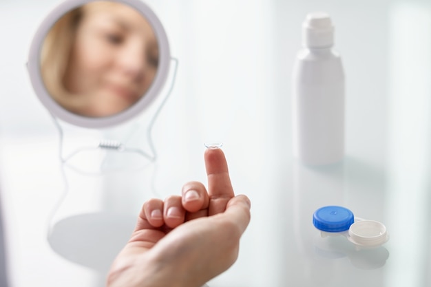 Une femme est assise devant un miroir et met des lentilles de contact sur ses yeux