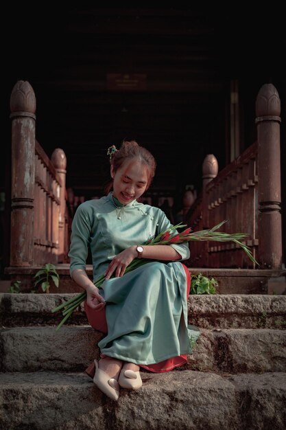 Une femme est assise sur un escalier de pierre et tient un bouquet de fleurs.
