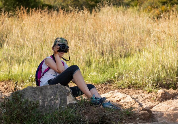 Une femme est assise sur un rocher et prend une photo de l'herbe derrière elle.