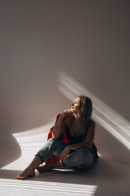 Une femme est assise sur un sol devant une fenêtre avec le soleil qui brille à travers la fenêtre.