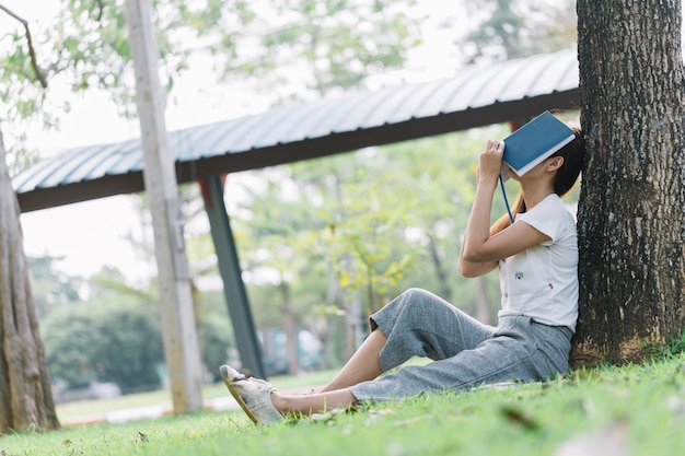 la femme est assise sous un arbre et elle apporte un livre pour couvrir son visage