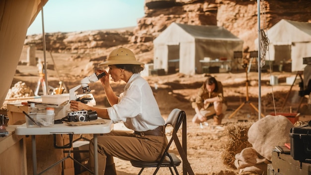 Photo une femme est assise à une table avec un microscope et un homme regarde un rocher en arrière-plan.